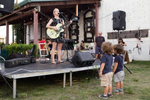 Two Children Enjoying Woman Sing and Play Guitar at Black Amethyst Tattoo Gallery Art Show